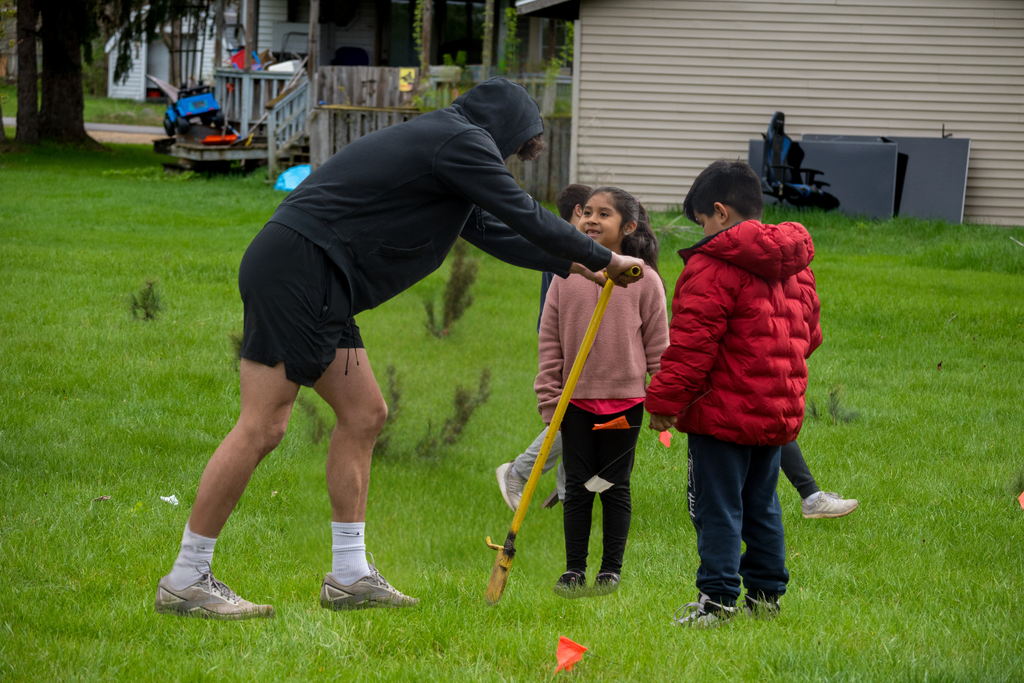 Excited students watching an older student create a hole to plant a tree 