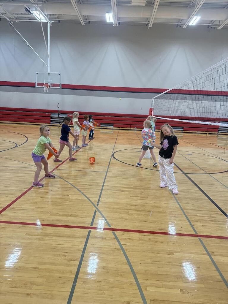Happy students working hard on their passing form in summer school in the gym 