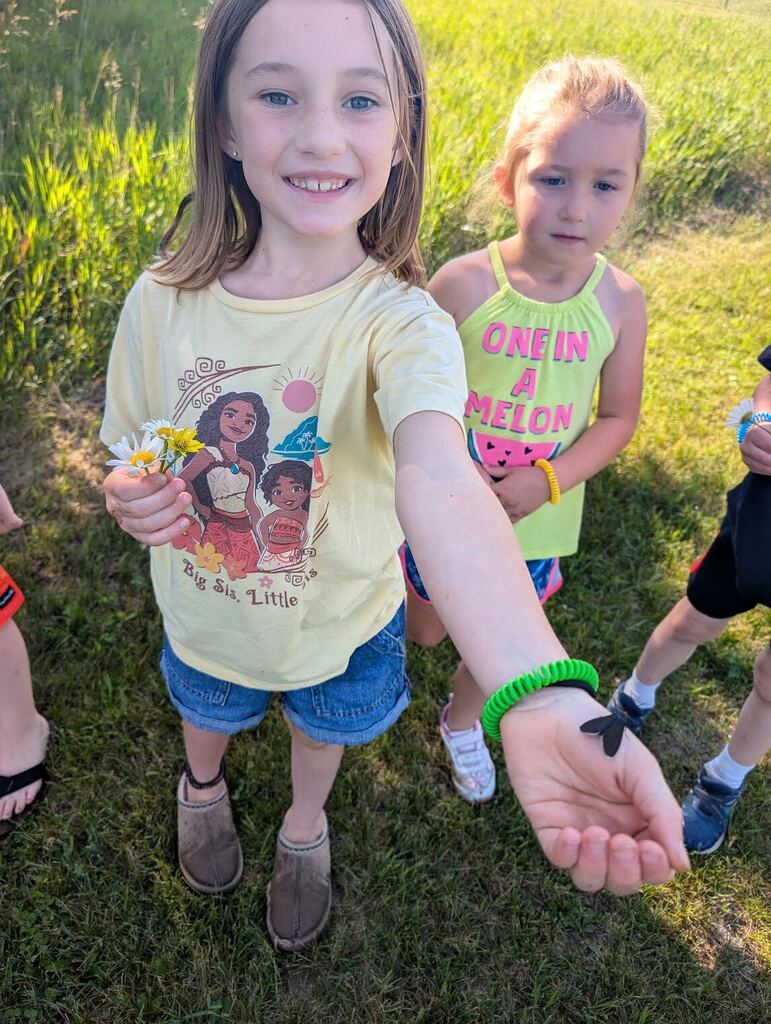 One student excitingly showing off the bug that they found while on the nature walk. Other students in the background looking at the bug as well. 