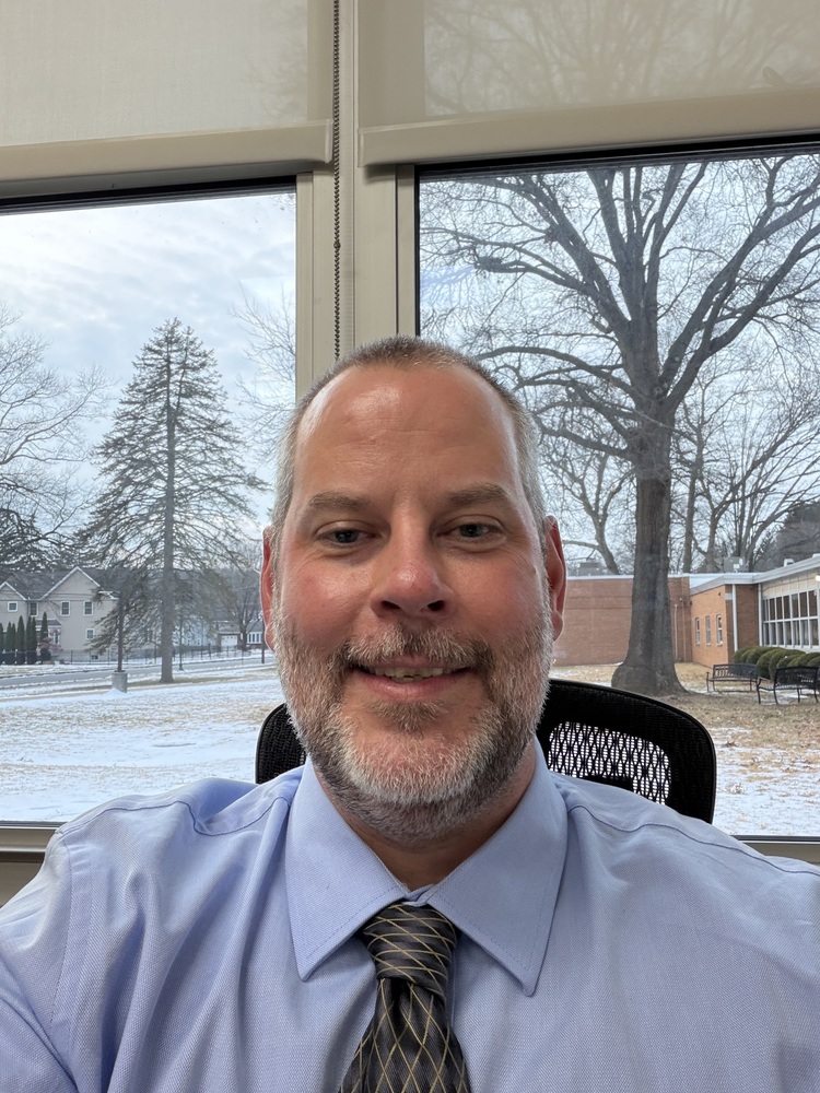 White man sitting at a computer chair infront of a window with snow on the ground