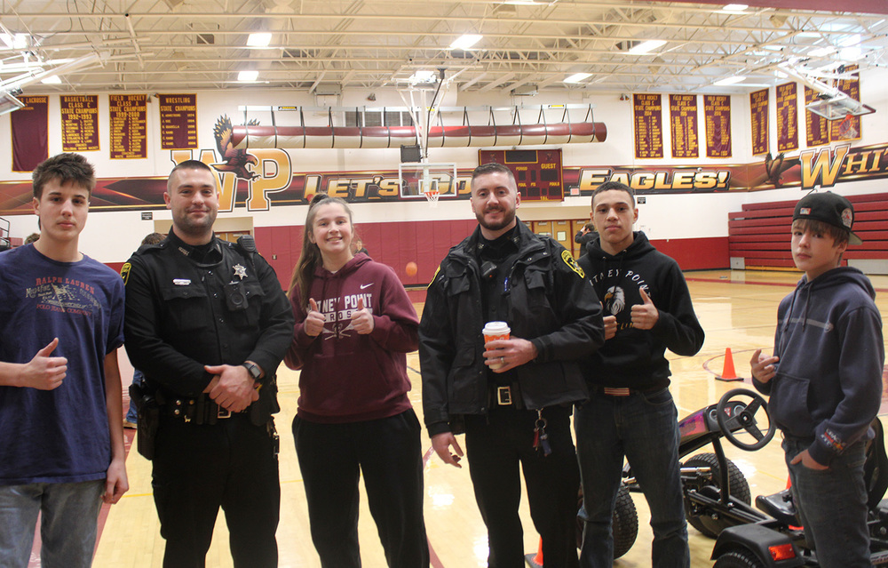 Whitney Point High School students making a thumbs up gesture as they stand with two officers from the Broome County Sheriffs Office in the high school gym.