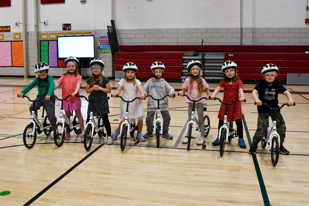 A row of first graders wearing helmets at Caryl E. Adams Primary school in Whitney Point are lined up with their bicycles in the school gym as they participate in a bike-riding lesson as part of the All Kids Ride program in their physical education class.