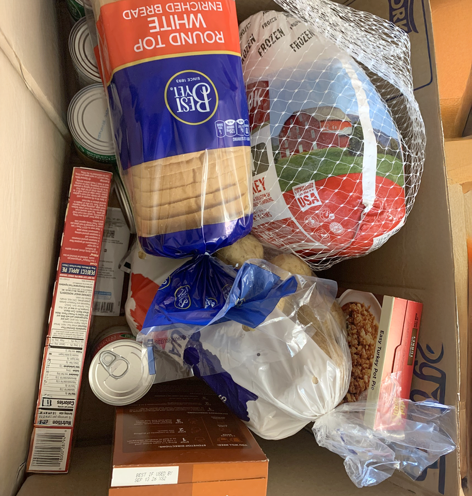 A box filled with supplies for a Thanksgiving meal, including a loaf of bread, turkey, stuffing mix and other cans or boxes that cannot be identified.