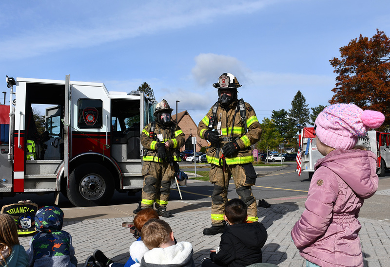 A fire fighter wearing gear speaks to young students at Caryl E Adams Primary School during a fire safety lesson.