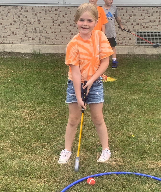 A Caryl Adams student practicing shooting a toy golf ball into a hulu hoop on the ground representing the hole.