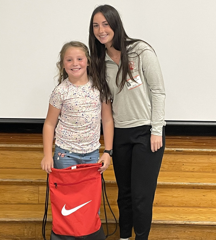 A Caryl Adams student holding a red cinch backpack with white Nike swoosh next to a SUNY Cortland student majoring in Physical Education.