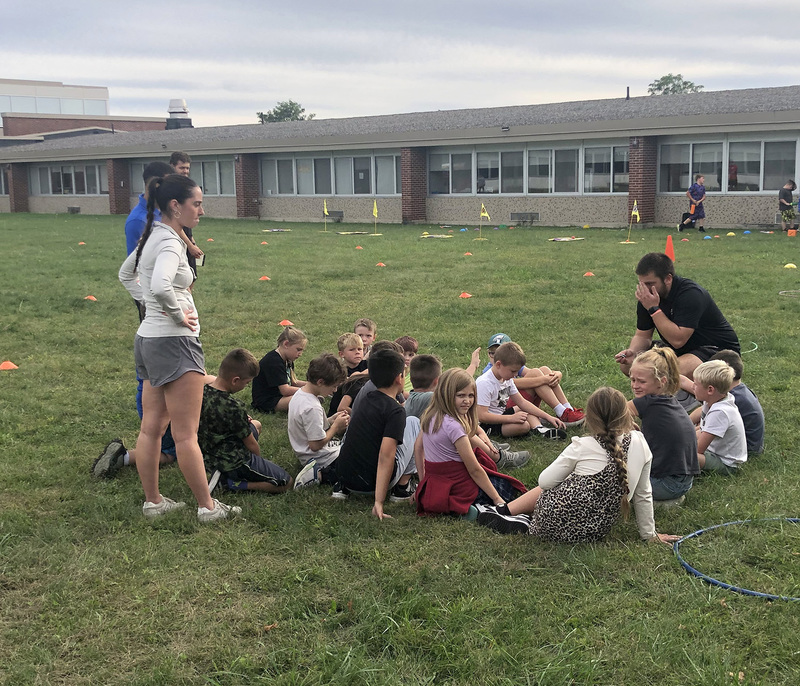 Caryl Adams students sit on the grass with Physical Education majors from SUNY Cortland as they are about to learn the rules of the next game they will try.
