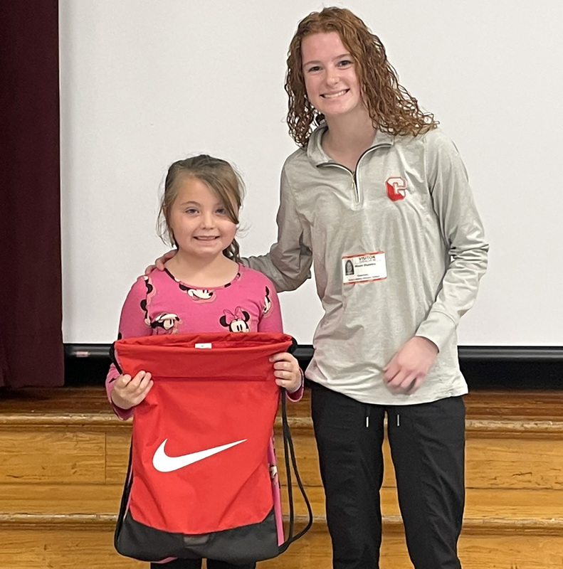 A Caryl Adams student holding a red cinch backpack with white Nike swoosh next to a SUNY Cortland student majoring in Physical Education.