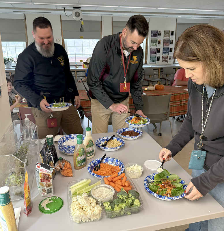 T R A  school resource officer, principal and another staff member add vegetables and cheese to their salads.