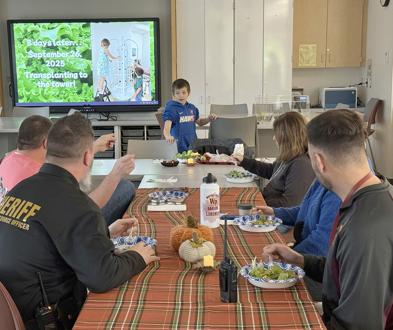 A fourth grader explains to guests about to sample their salads made with lettuce grown by him and his classmates, the process of planting and growing the produce.