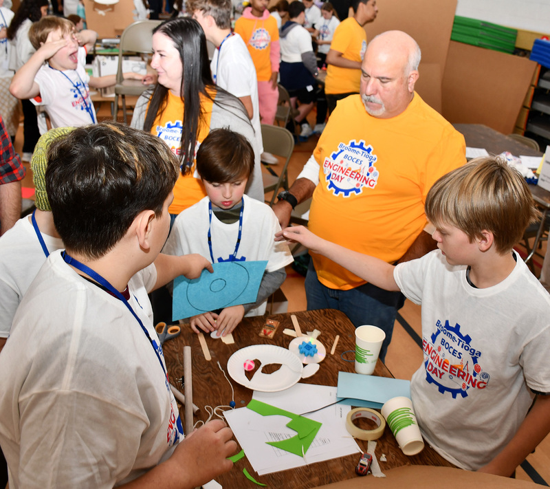 T R A students in the process of building their Rube Goldberg machine as an Engineering Day judge watches.