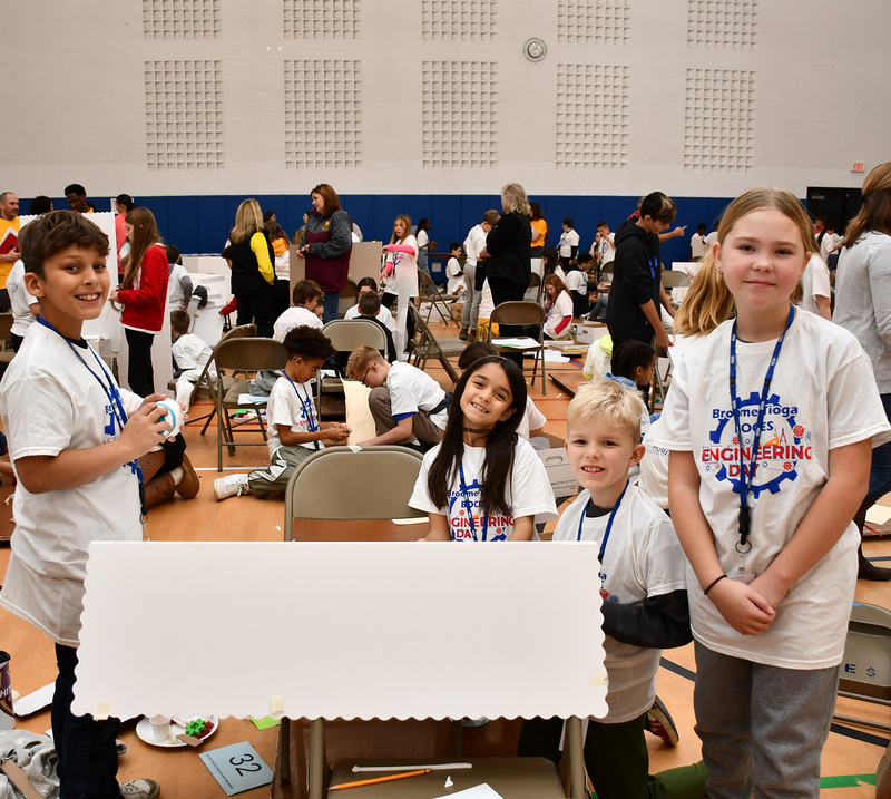 Four T R A students on a different team with the machine they are building for the Elementary Engineering Day competition on November 20, 2025.