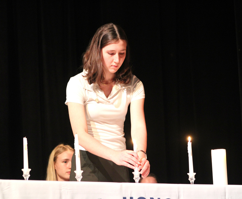 The secretary of the Whitney Point High School National Honor Society chapter sets a white candle into its holder.
