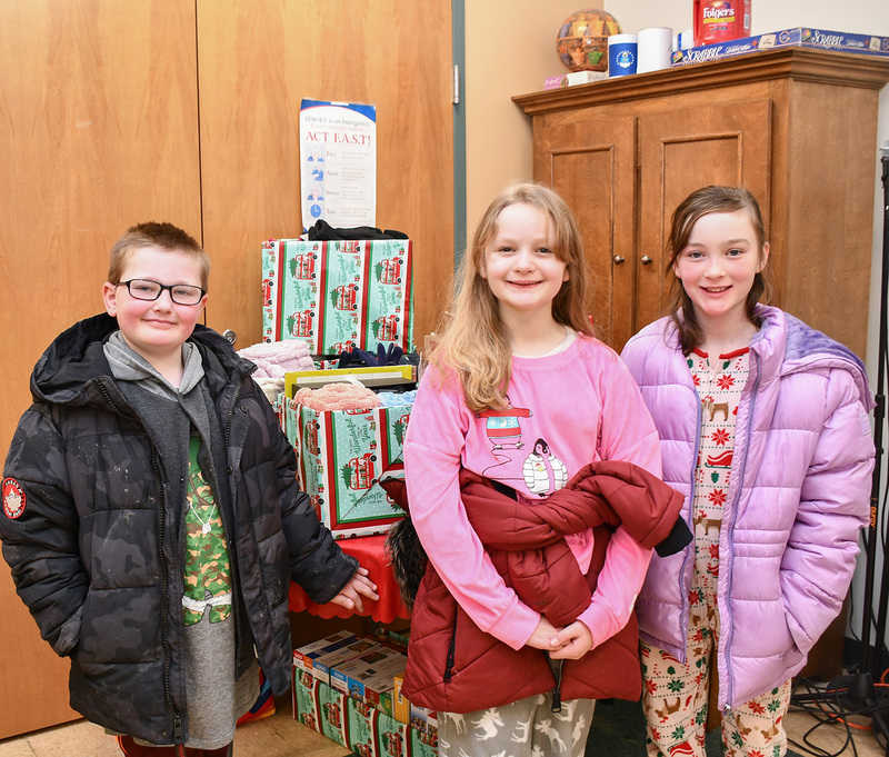 Three fourth graders by the boxes of gifts they helped collect to give to Senior Center patrons.
