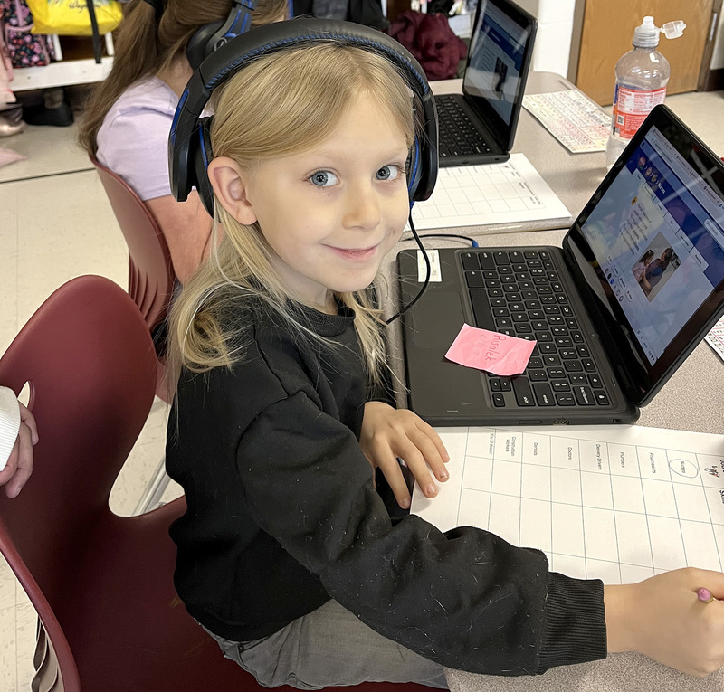 A Caryl E. Adams Primary school student wearing headphones works on a laptop as she fills in a chart about careers.