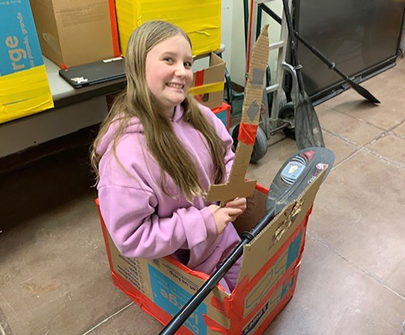 A student in a cardboard boat holds a cardboard sword that looks like a pirate's sword.