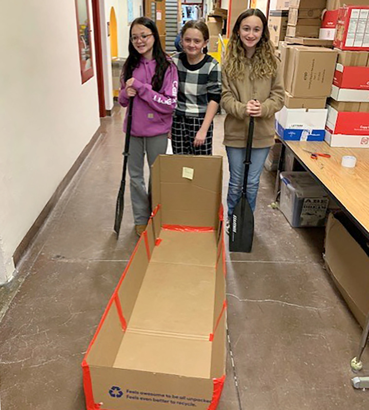 Three students stand behind the boat they made out of cardboard and waterproof duck tape.