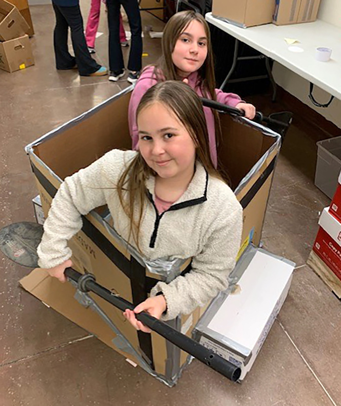 Two students sit in their cardboard boat.