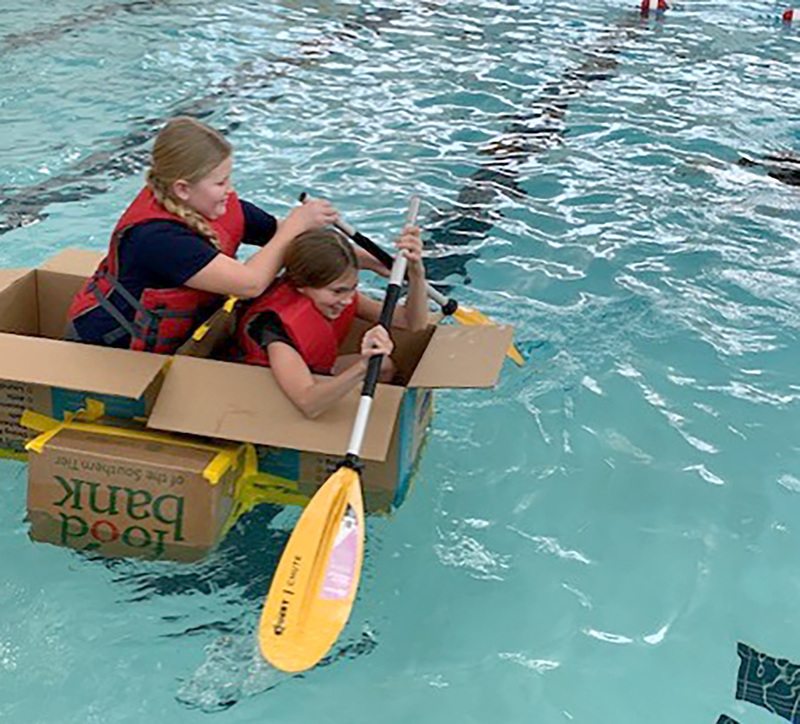 Two students giggle as they continue to paddle across the Whitney Point swimming pool in their boat created out of cardboard and duct tape.
