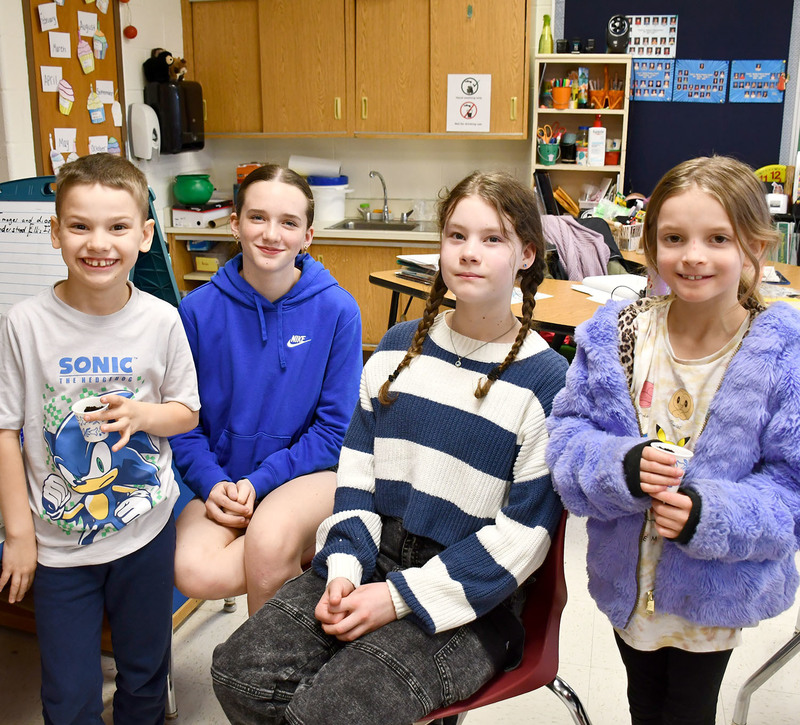 Two second graders stand next to two Tioughnioga Riverside Academy students from the Agrictultural Technology class holding cups of dirt with grass seeds that they planted in them.