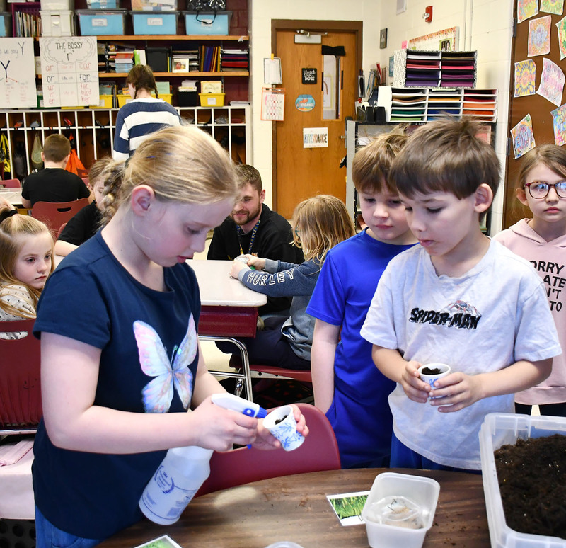 Two second graders watch as another waters her planted grass seed with a spray bottle.