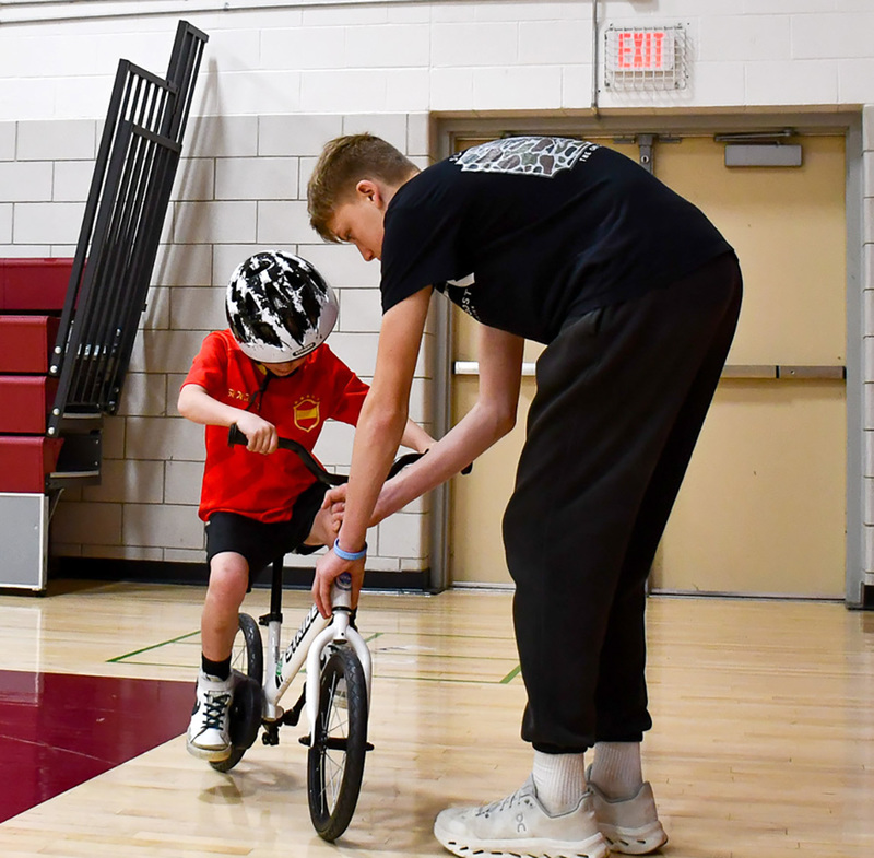 A Whitney Point High School ninth grader helps a first grader balance on a bicycle as he learns to ride in his physical education class at Caryl Adams Primary.