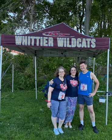 Mrs. Bucher, Ms. Bragg, and Mr. Cunningham smiling together under the Whittier Wildcats tent after running the Flag Day 5k.