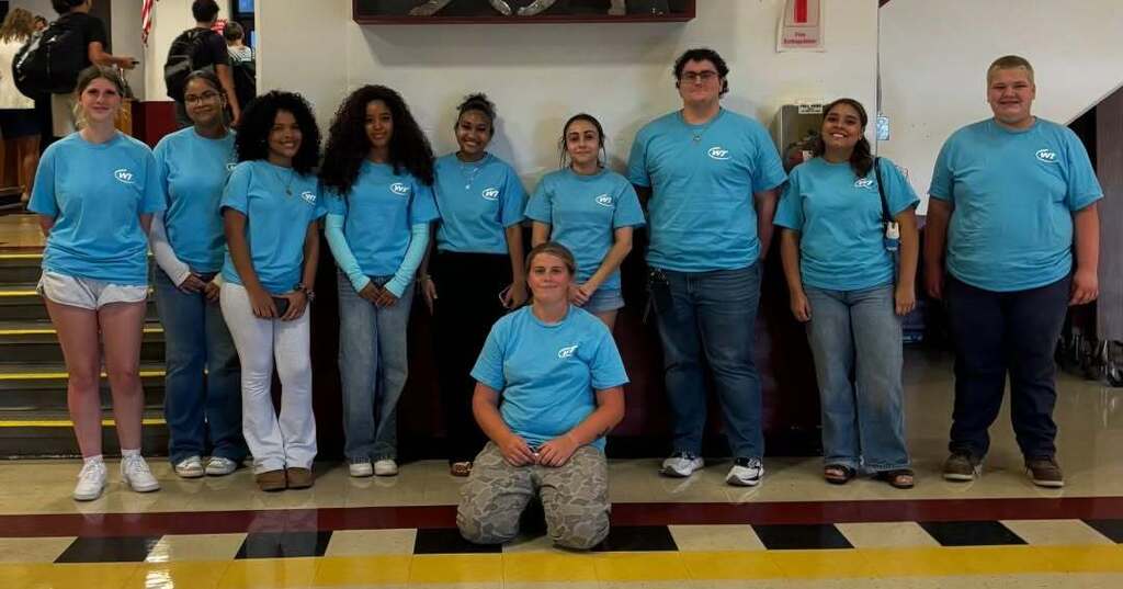 A group of Student Leaders stand behind one Student Leader kneeling on the ground.
