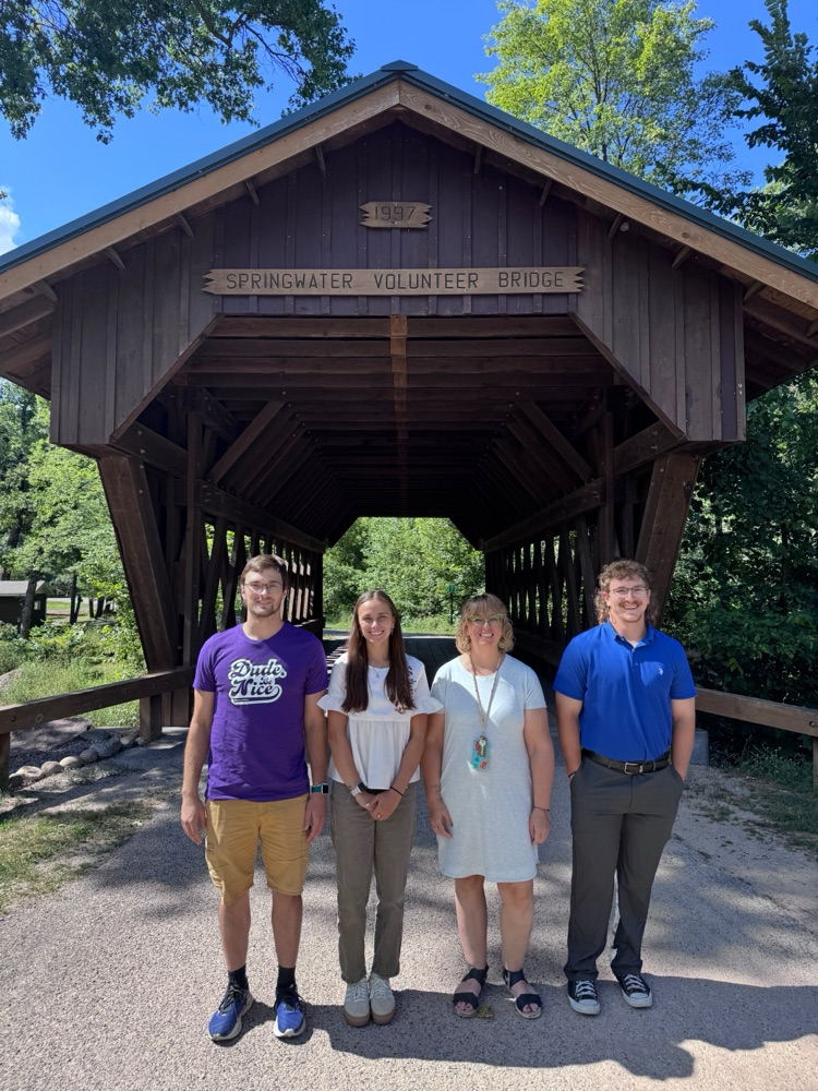 four new staff members stand in front of covered bridge