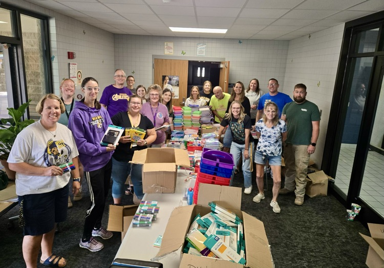 Wild rose and evergreen staff stand by donated school supplies