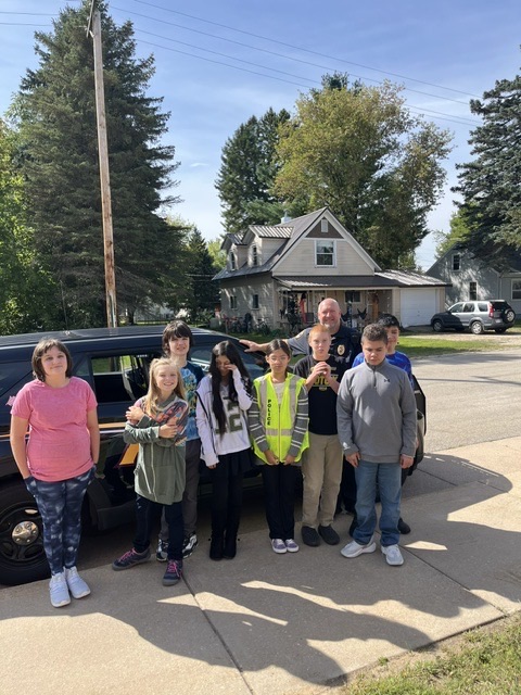 Middle school students stand in front of squad car with Chief Klapoetke