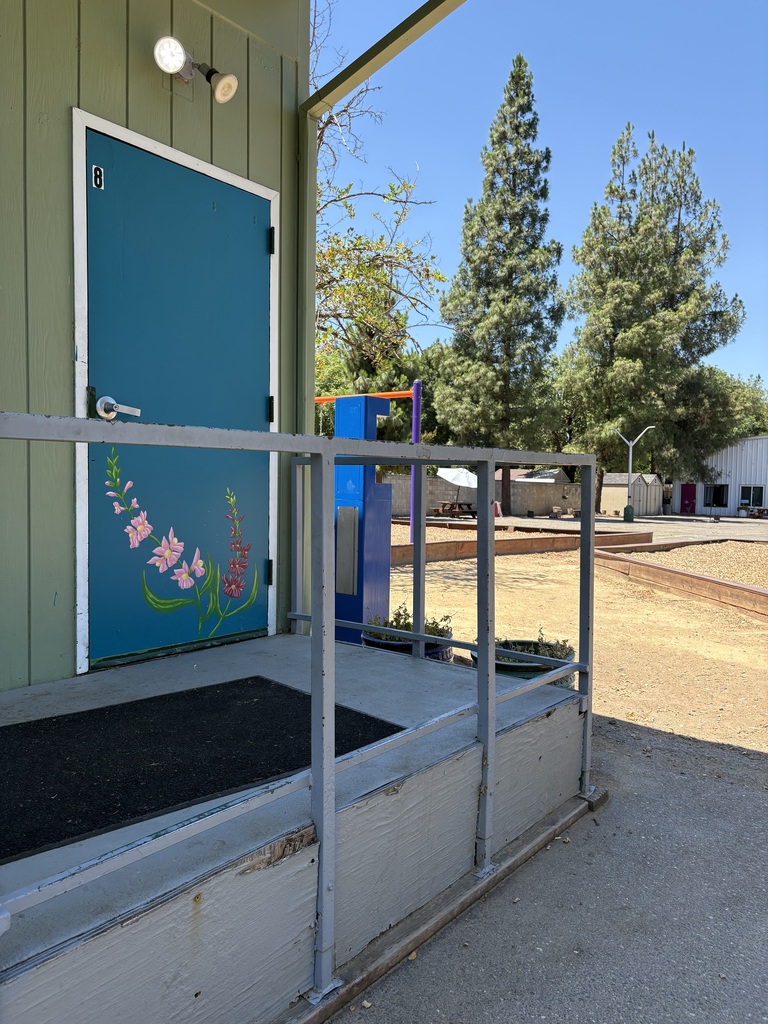 A photo of one of our WOCAP classrooms with a flower mural on the door and the playground in the background.