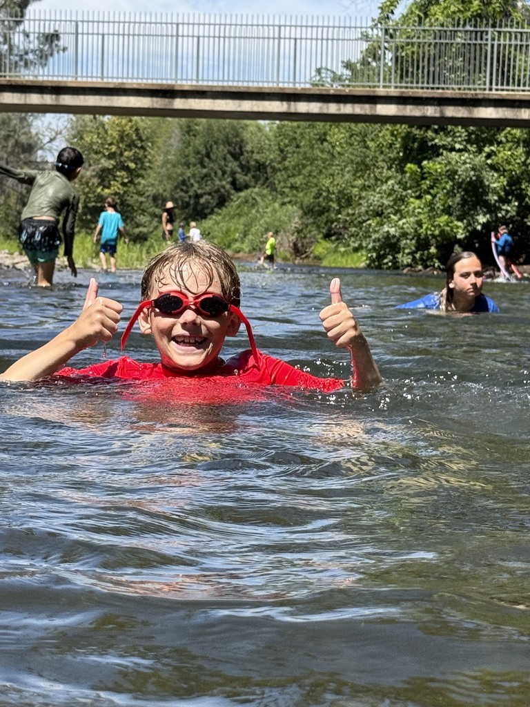 One student giving two thumbs up while swimming in the creek with his goggles on.