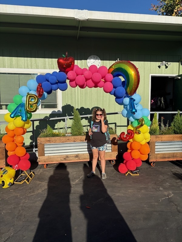 A photo of a student standing under a rainbow balloon arch that was set up for the first day of school.