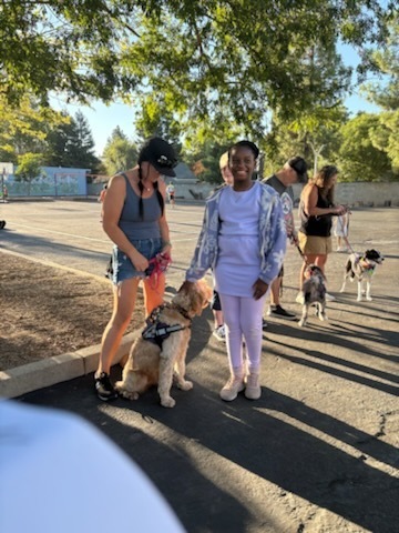 A photo of one of our students saying hi and petting one of the therapy dogs. She is smiling and very happy to see the dog, Winston.
