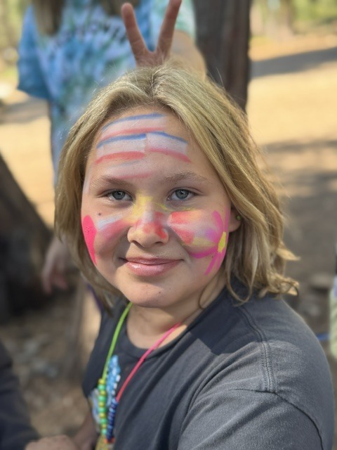 A close-up photo of a student who has had some face paint done. She has a flower on one cheek and a heart on the other. She also has French flags on her forehead.