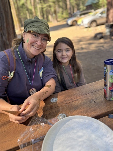 A photo of our WOCAP teacher, Melissa sitting at a picnic table with a student. Both of them are smiling for the camera.