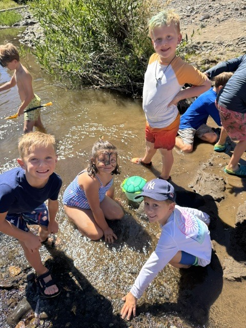 Here is a photo of a group of students playing and exploring in the creek. They are all looking up at the camera and smiling.