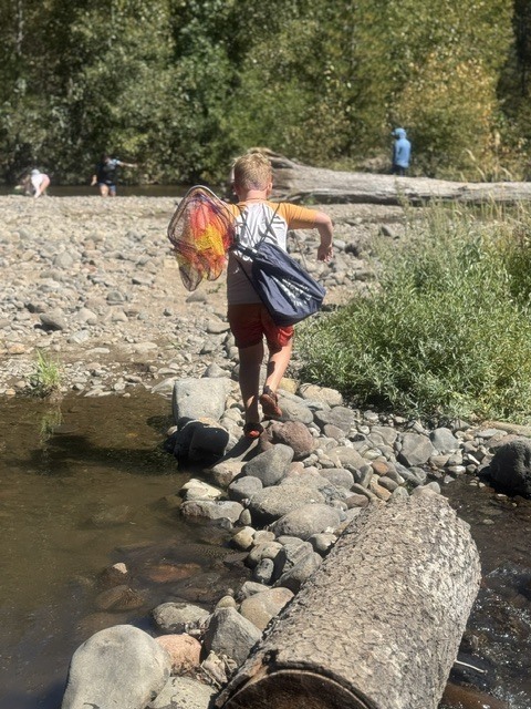 Here is a photo taken behind a student who is walking across a log over the creek.