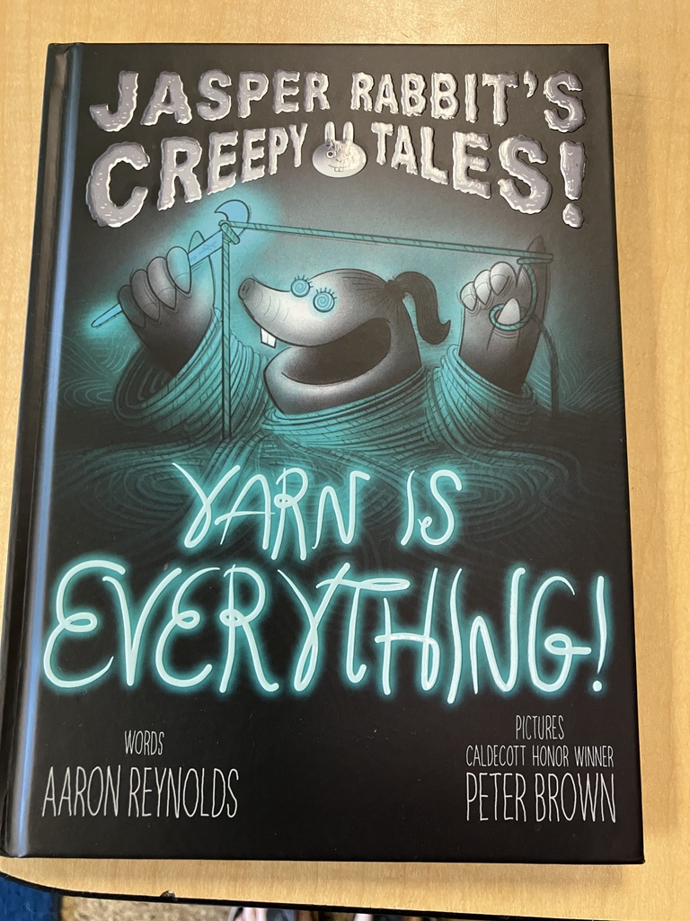 Here is a photo of a book titled "Jasper Rabbit's Creepy Tales! Yarn is Everything!" This book cover is black with blue-colored illustrations. At the top is the text "Jasper Rabbit's Creepy Tales!" Underneath that is a drawing of a rabbit all wrapped up in blue yarn. The rabbit is grey with black details. Underneath the drawing is the text "Yarn is Everything" in blue writing, mimicking the look of the yarn. At the bottom is the name of the author and illustrators in the left and right corners.