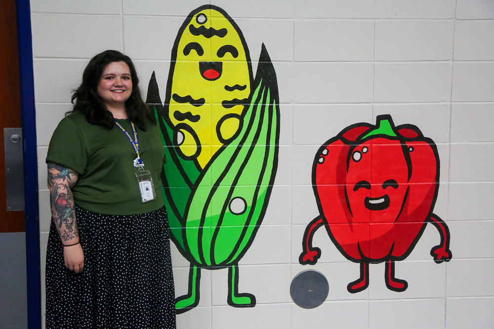 Hannah Grube art teacher with artwork completed in the cafeteria at WCPES