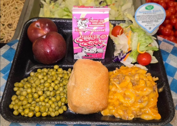 High school lunch tray featuring cheeseburger mac, sweet peas, a whole-grain dinner roll, fresh plums, side salad with cherry tomatoes, ranch dressing, and strawberry milk.