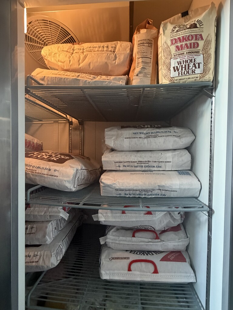 Several large bags of flour stacked in a fridge for future class use