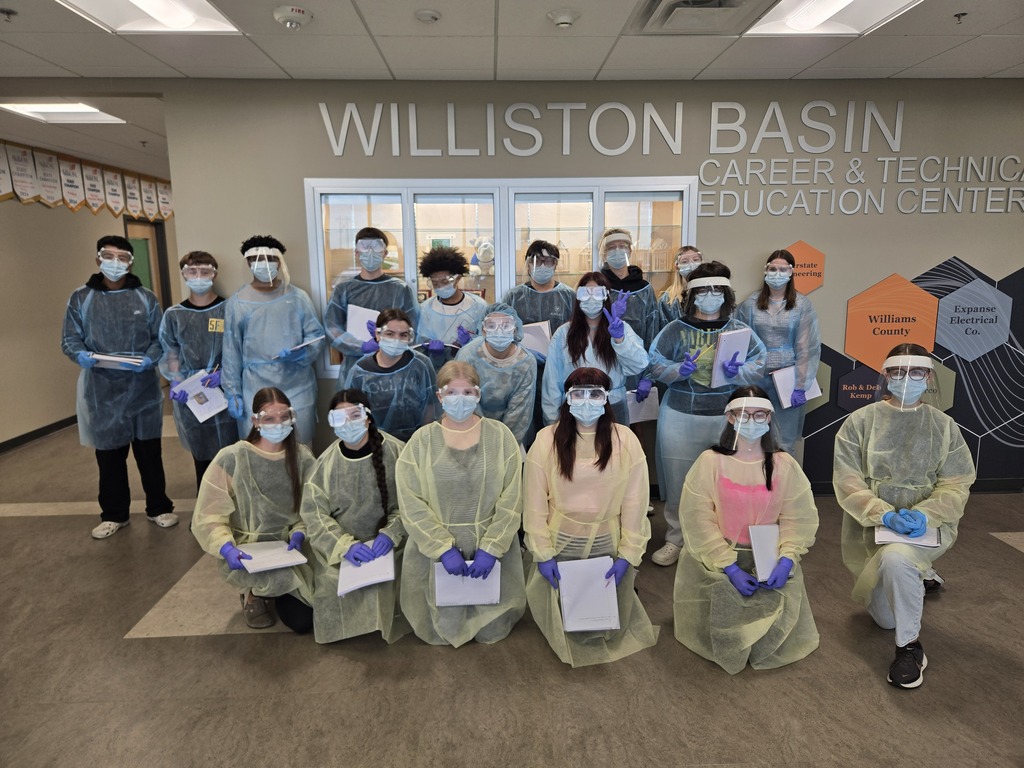 19 students dressed in blue or yellow PPE gear standing in a group