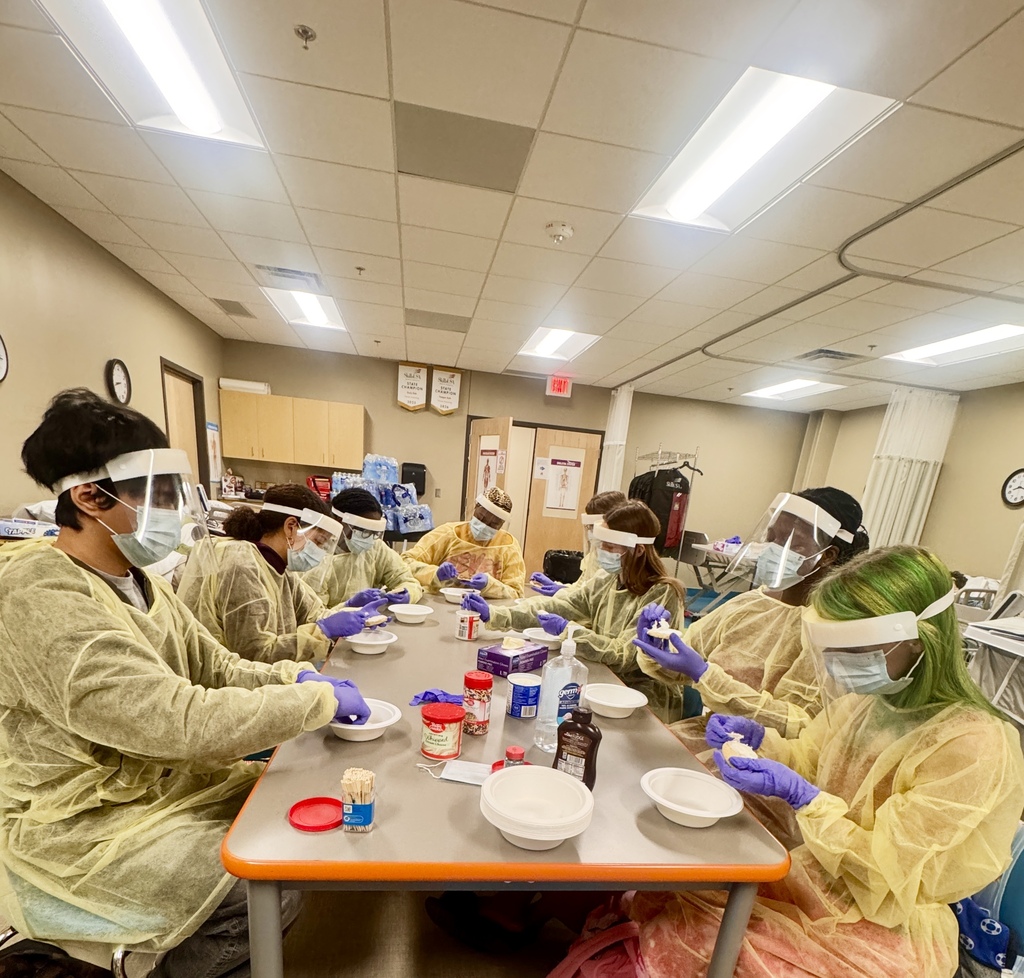 8 students in PPE gear decorating cookies with icing