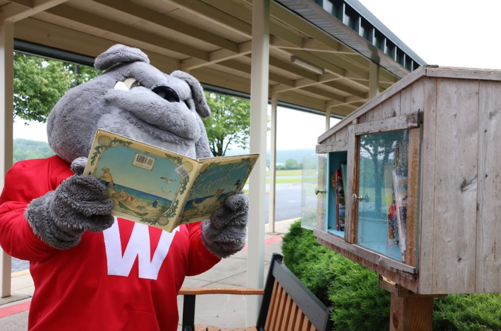 Bulldog reading book outside of little library