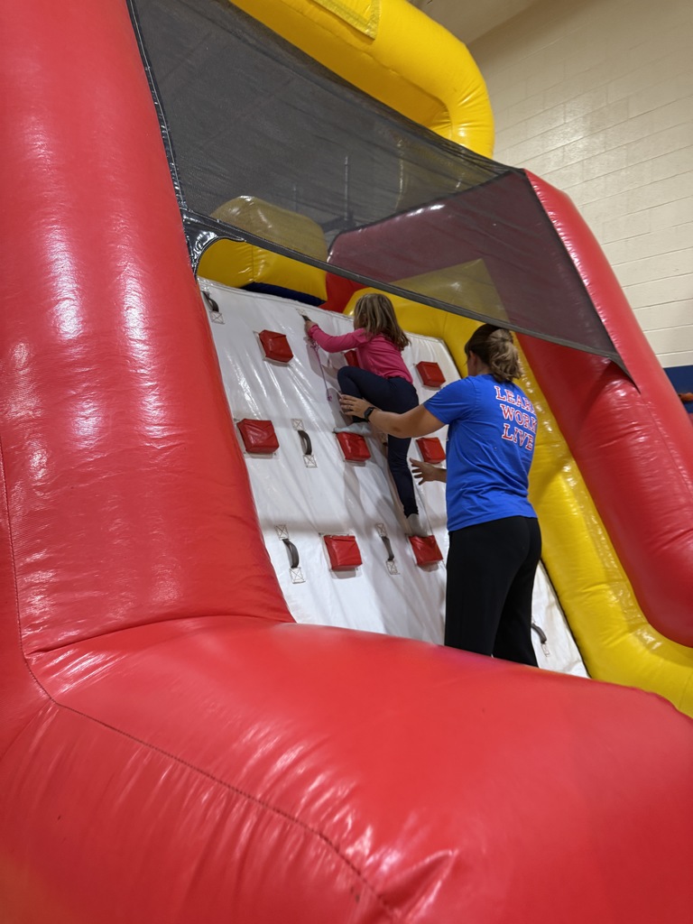 student climbing up wall with teachers help