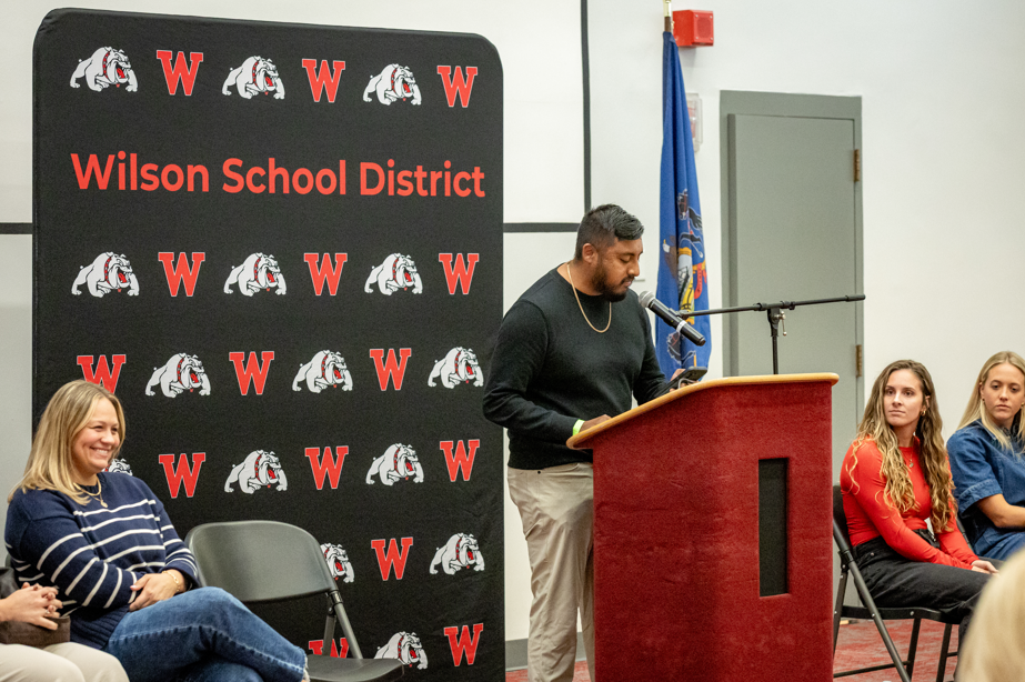 man speaking at thepodium with people smiling on sides
