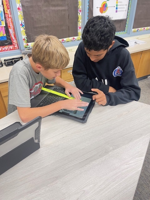 two students working together while measuring with ruler on cromebook