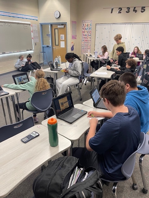 students are seen working at desks in pairs while jotting down notes as well as measuring and analyzing project features on cromebooks